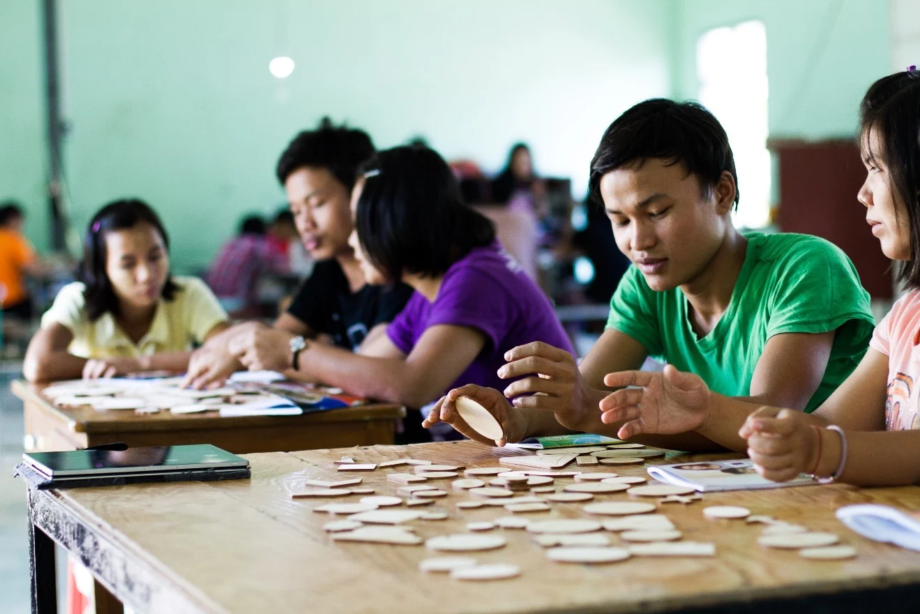 Young people in Myanmar work together with visual storytelling pieces around a table.
